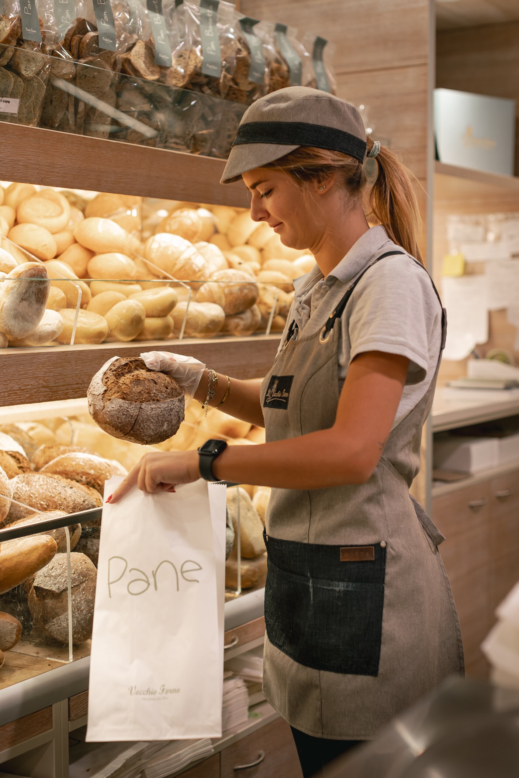 Commessa del Vecchio Forno mette una pagnotta nel sacchetto Pane