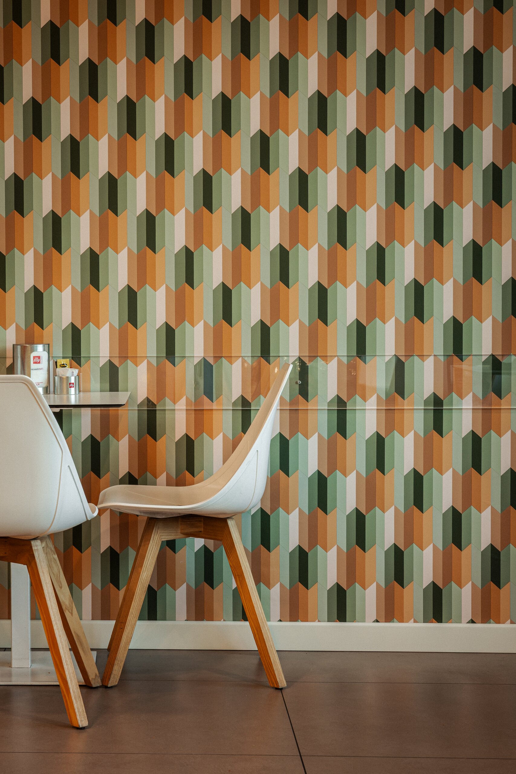 Parete a motivo geometrico verde e arancio con sedie bianche dalle gambe in legno al Vecchio Forno